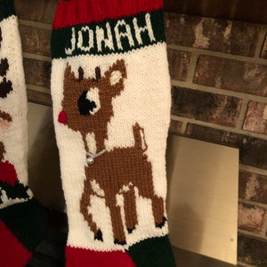 Puede incluir: Una media de Navidad de punto roja, blanca y verde con un diseño de reno y el nombre "JONAH" bordado en el puño.
