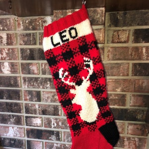 May include: Red and black plaid Christmas stocking with a white deer design and the name "LEO" embroidered on the cuff.