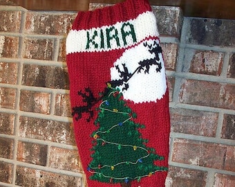 May include: Red and white knitted Christmas stocking with the name "Kira" embroidered on the cuff. The stocking features a green Christmas tree with white lights and a reindeer pulling a sleigh with a white moon in the background.