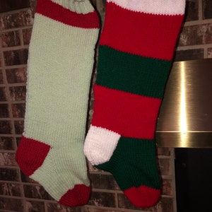 May include: Two knitted Christmas stockings hanging on a brick fireplace mantel. One stocking is green and white with red accents, and the other is red and green with white accents.