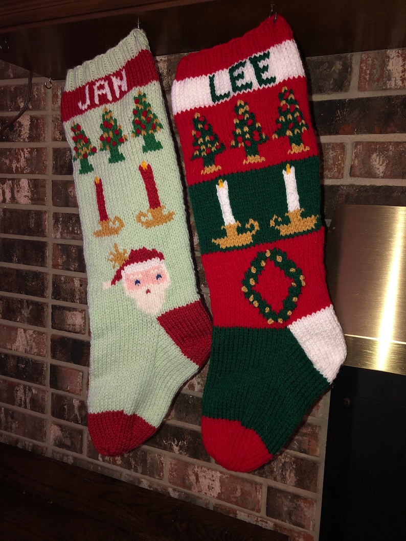 May include: Two knitted Christmas stockings with red, green and white stripes. The stocking on the left has the name "Jan" embroidered on it and a Santa Claus face. The stocking on the right has the name "Lee" embroidered on it and a wreath.