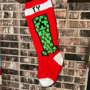 Könnte beinhalten: Rote und weiße gestrickte Weihnachtsstrumpf mit einer grünen Minecraft Creeper Figur und dem Namen "TY" am Bündchen.