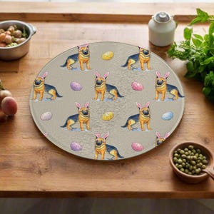 May include: A circular glass chopping board with a repeating pattern of German Shepherds wearing bunny ears and Easter eggs. The board has a tan background and is suitable for kitchen use.