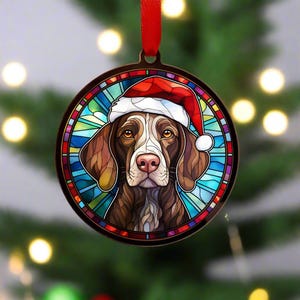 May include: A stained glass style Christmas ornament featuring a brown and white German Shorthaired Pointer dog wearing a red Santa hat. The ornament is round and has a blue, green, and red background.