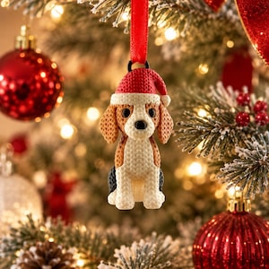 Könnte beinhalten: Ein Beagle-Hundeornament mit einer strukturierten, strickartigen Oberfläche, das eine rot-weiße Weihnachtsmannmütze trägt. Der Hund hat braune, weiße und schwarze Abzeichen, große dunkle Augen und eine schwarze Nase. Es hängt an einer roten Schleife.
