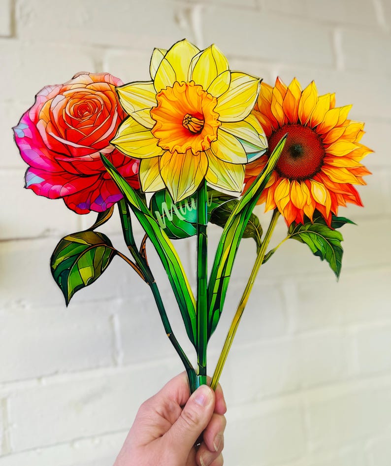 May include: A bouquet of three paper flowers, a red rose, a yellow daffodil, and an orange sunflower. The flowers are hand-painted and have a stained glass look.