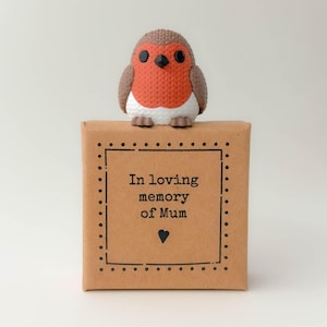 Könnte beinhalten: Eine braune Geschenkbox mit dem Text "In loving memory of Mum" und einem kleinen schwarzen Herz. Eine dekorative Rotkehlchen-Figur mit roter Brust, braunen Flügeln und weißem Bauch sitzt auf der Box.