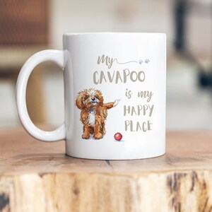 Può includere: Una tazza in ceramica bianca con un'illustrazione marrone e bianca di un cane cavapoo con una palla rossa. Il testo sulla tazza recita "My Cavapoo is my happy place."