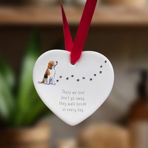 May include: White ceramic heart-shaped ornament with a brown and white dog illustration and the text "Those we love don't go away, they walk beside us every day".