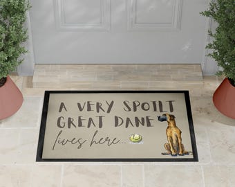 May include: Rectangular doormat with a black border and the text "A VERY SPOILT GREAT DANE lives here...". The mat features a watercolor illustration of a Great Dane dog and a tennis ball.