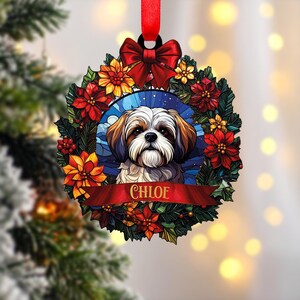 Può includere: Ornamento natalizio rotondo con un cane Shih Tzu e il nome "CHLOE" su uno striscione rosso. Il cane è circondato da una ghirlanda di fiori rossi e gialli e foglie verdi, con un fiocco rosso in alto. Un nastro rosso è attaccato per appenderlo.