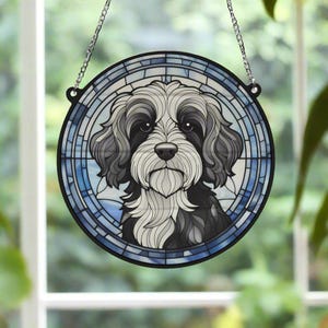 Pode incluir: Uma janela de vitral pendurada com um design azul e branco apresentando um cão preto e branco com uma pelagem felpuda.