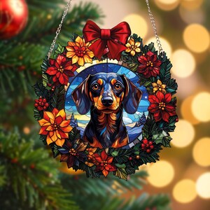 Könnte beinhalten: Ein runder Weihnachtsschmuck mit einem Dackel im Buntglasstil. Der Hund ist von einem Kranz aus roten und gelben Blumen, grünen Blättern und einer roten Schleife umgeben. Der Schmuck hängt an einer silbernen Kette.