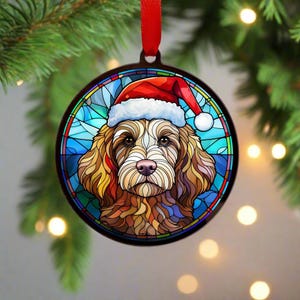 Könnte beinhalten: Ein Weihnachtsornament aus Buntglas mit einem Hund, der einen Weihnachtsmann-Hut trägt. Der Hund ist braun und weiß vor blauem Hintergrund.