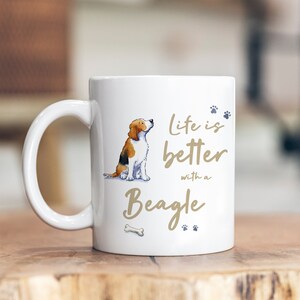 May include: White ceramic mug featuring a brown and white beagle illustration. The mug displays the text "Life is better with a Beagle" in brown lettering with paw prints.