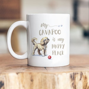 Könnte beinhalten: Weiße Keramiktasse mit einer braunen Illustration eines Cavapoo-Hundes, der mit einem roten Ball spielt. Der Text auf der Tasse lautet "My Cavapoo is my happy place."