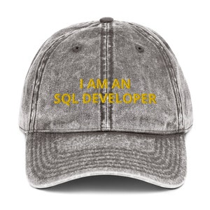 Puede incluir: Una gorra de béisbol de estilo vintage, de color gris, con el texto "I AM AN SQL DEVELOPER" bordado en amarillo.