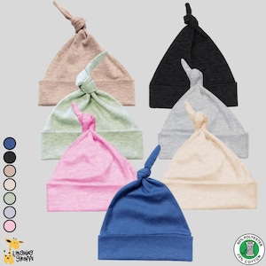 May include: A collection of six baby knot hats in various colors: pink, blue, green, beige, gray, and black. The hats are made of a soft fabric and feature a knotted top. The Laughing Giraffe logo and fabric content are visible.