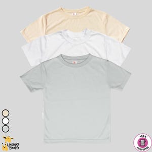 May include: Three short-sleeved t-shirts in cream, white, and light gray are stacked on a light gray background. The shirts have a crew neck and a small logo on the upper chest. The bottom right corner has a 100% polyester label.