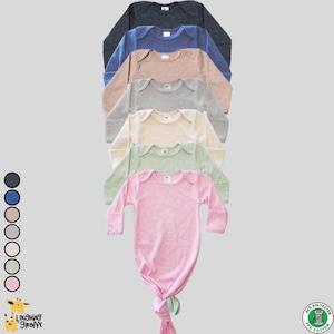 Puede incluir: Una pila de siete batas de bebé con nudo y manga larga en varios colores, incluyendo azul marino, azul claro, beige, gris, verde claro y rosa. Las batas están hechas de 65% poliéster y 35% algodón.