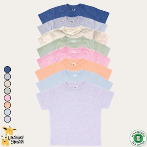 Puede incluir: Una pila de camisetas de manga corta en varios colores pastel, incluyendo azul, gris, beige, verde, rosa, naranja y lavanda. Las camisetas están hechas de una mezcla de poliéster y algodón. El logo "Laughing Giraffe" es visible.