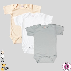 May include: Three short-sleeved baby onesies in beige, white, and light gray. The onesies are made of 100% polyester.