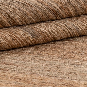 May include: Close-up of a natural fiber rug with a woven texture. The rug is a light brown color with a subtle pattern.