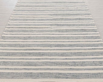 Puede incluir: Una alfombra de rayas blancas y azules con textura tejida. La alfombra tiene un brillo sutil y está hecha de fibras naturales.