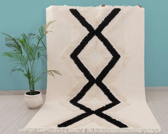 May include: A white and black geometric patterned rug with a fringe border. The rug has a fluffy texture and features a bold black and white diamond pattern.