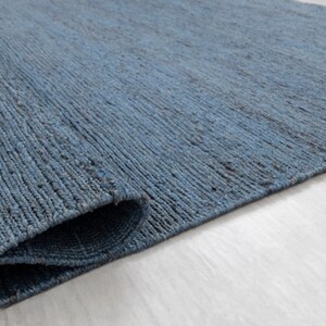 May include: A close-up of a blue woven rug with a textured surface. The rug is folded in half and the edges are visible.