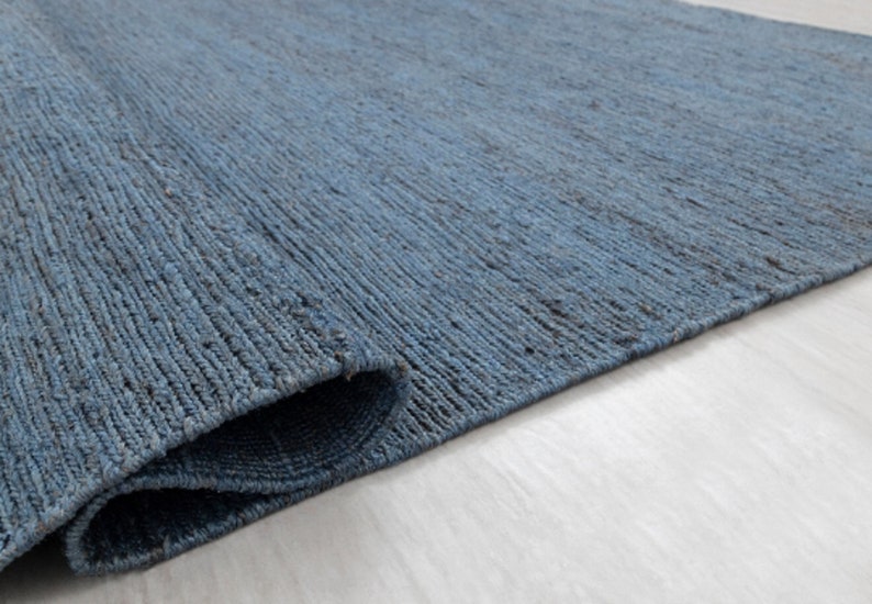 May include: A close-up of a blue woven rug with a textured surface. The rug is folded in half and the edges are visible.