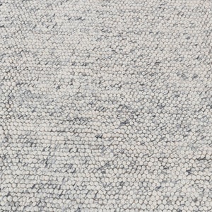 May include: Close-up of a white and gray textured rug with a circular pattern. The rug is made of small, round, woven fibers.