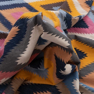 May include: A colorful woven fabric with a geometric pattern in shades of blue, yellow, pink, and brown. The fabric is folded and draped, creating a textured and abstract design.