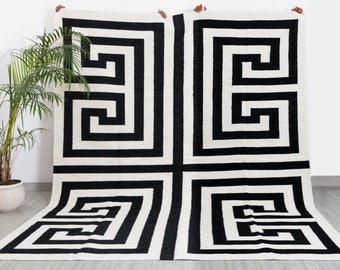 Puede incluir: Alfombra de área negra y blanca con un patrón geométrico de llave griega. La alfombra está hecha de un material suave y mullido y tiene un diseño moderno.