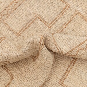 May include: A cream-colored rug with a geometric pattern woven in a darker beige color. The rug is folded in half, showing the texture of the woven fibers.