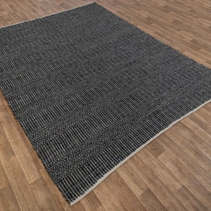 Op de afbeelding: Een zwart-wit geweven tapijt met een geometrisch patroon. Het tapijt heeft een subtiele glans en een licht getextureerd oppervlak.