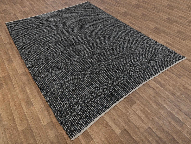 Op de afbeelding: Een zwart-wit geweven tapijt met een geometrisch patroon. Het tapijt heeft een subtiele glans en een licht getextureerd oppervlak.