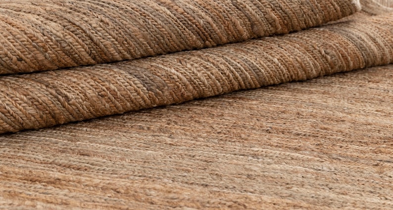 May include: Close-up of a natural fiber rug with a woven texture. The rug is a light brown color with a subtle pattern.