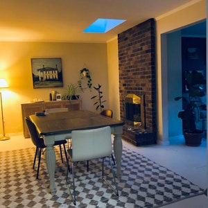 May include: A dining room with a wooden table and chairs, a brick fireplace, and a skylight. The table is set with a white tablecloth and a vase of flowers. The fireplace is decorated with a painting of a house.
