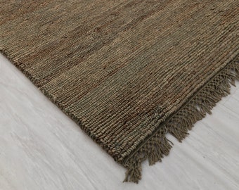 May include: A close-up of a natural fibre rug with a fringe border. The rug is a light brown colour with a subtle green hue.