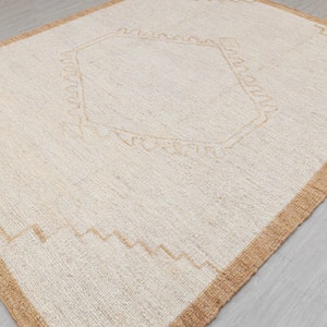 May include: A white rug with a beige border and a geometric design in the center.