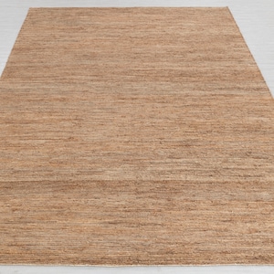 May include: A brown and beige woven rug with a subtle striped pattern. The rug is made of natural fibers and has a rustic, earthy look.
