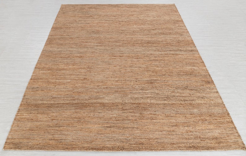 May include: A brown and beige woven rug with a subtle striped pattern. The rug is made of natural fibers and has a rustic, earthy look.