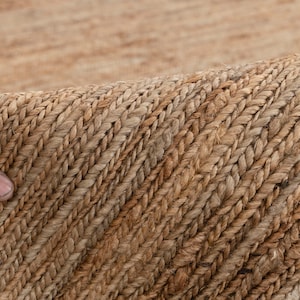 May include: Close-up of a natural fiber rug with a woven texture. The rug is a light brown color and has a subtle pattern.