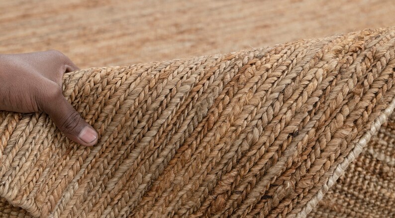May include: Close-up of a natural fiber rug with a woven texture. The rug is a light brown color and has a subtle pattern.