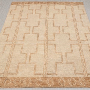 May include: A beige rug with a geometric pattern of brown crosses. The rug has a brown border with a diamond pattern.