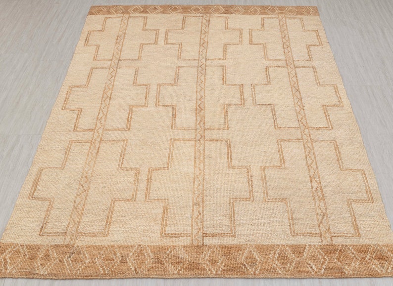 May include: A beige rug with a geometric pattern of brown crosses. The rug has a brown border with a diamond pattern.