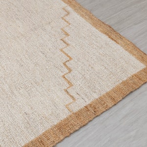 May include: A close-up of a natural fiber rug with a beige and brown border. The rug has a woven texture and a simple design.