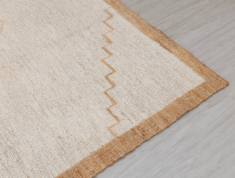 May include: A close-up of a natural fiber rug with a beige and brown border. The rug has a woven texture and a simple design.
