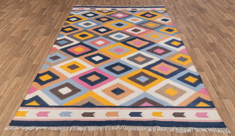 May include: A colorful geometric rug with a diamond pattern in shades of blue, pink, yellow, brown, and white. The rug has a navy blue border with a white and pink stripe.